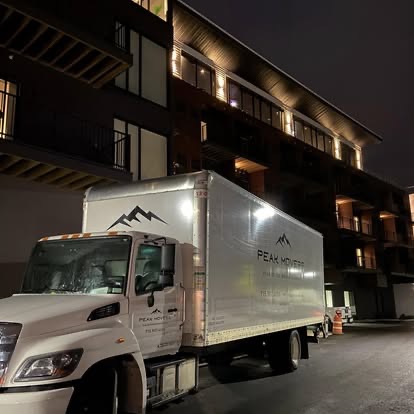 Peak Movers truck outside a modern apartment building in the evening